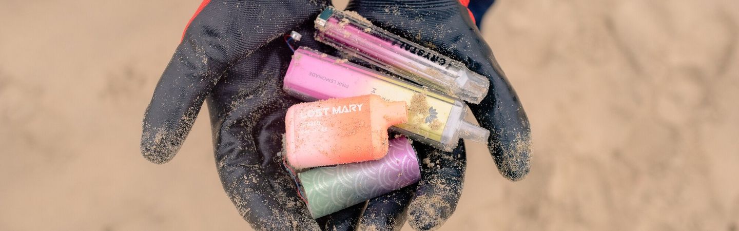 A pair of gloved hands holding multiple-coloured vapes. The photo is from a top down view.