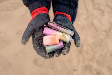 A pair of gloved hands holding multiple-coloured vapes. The photo is from a top down view.