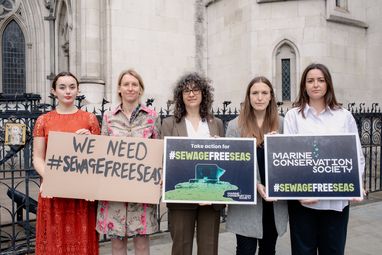 5 members of the Marine Conservation Society team standing outside Royal courts of Justice, holding signs that read 'Sewage Free Seas'. Sandy Luk, the CEO stands in the middle.