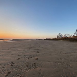 Blackpool beach with footprints in the sand. A rollercoaster is in the background as part of the pleasure park