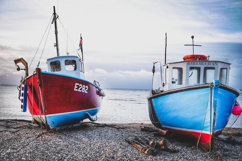A close up of two fishing boats resting on pebbles. One boat is a vivid red colour, and the other is a bright blue colour.