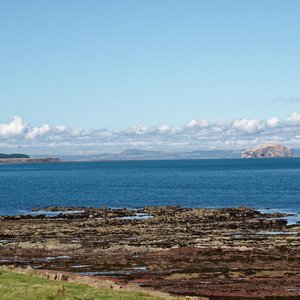 A view out over the Firth of Forth with a rocky shore in the foreground and a beautiful view across the water. The sky is blue and the clouds sit low in the sky.