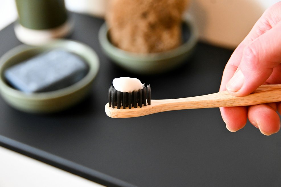 A hand holding a bamboo toothbrush with toothpaste on the end