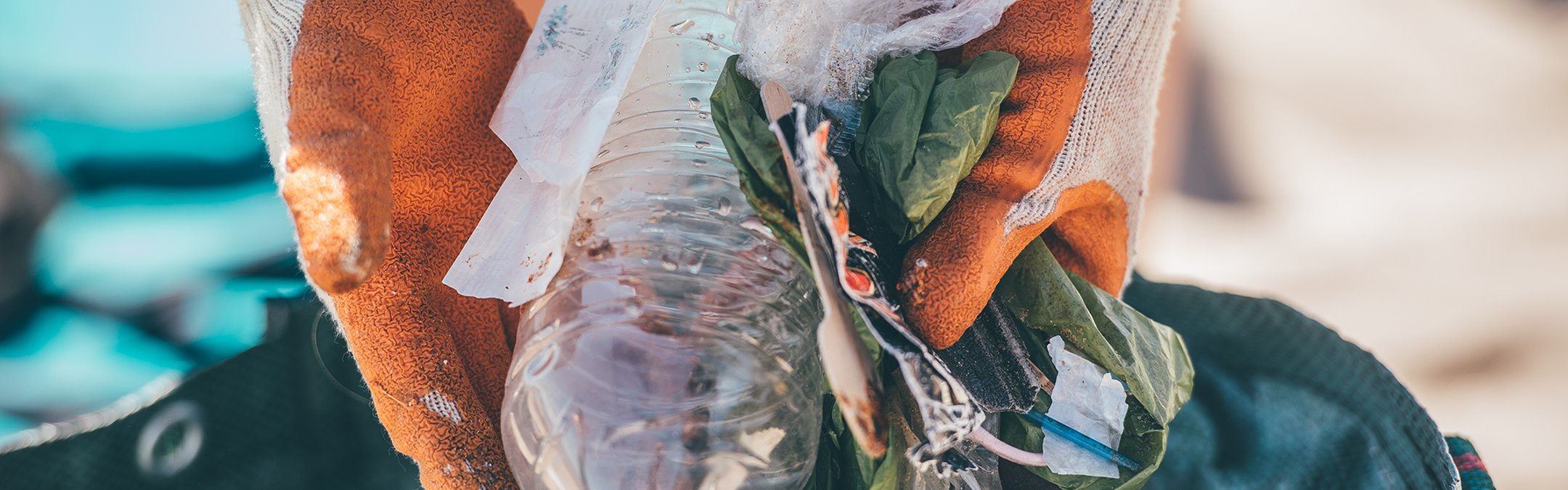A pair of gloved hands holds a selection of plastic litter above a bag. The plastic litter was found during a beach clean