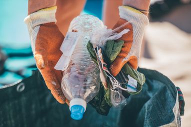 A pair of gloved hands holds a selection of plastic litter above a bag. The plastic litter was found during a beach clean