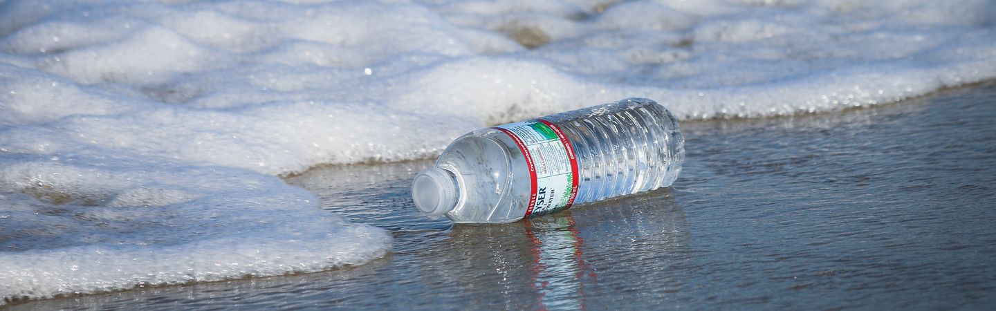 A plastic bottle is photographed on the shoreline, about to be washed away into the ocean
