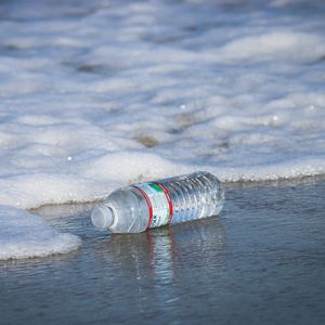 A plastic bottle is photographed on the shoreline, about to be washed away into the ocean