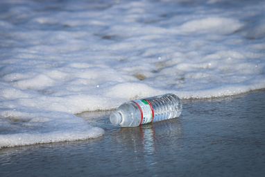 A plastic bottle is photographed on the shoreline, about to be washed away into the ocean