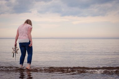 a person standing at the edge of the sea while holding a pair of shoes