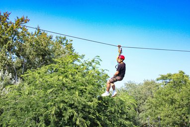 A man on a zipline, the trees can be seen below him