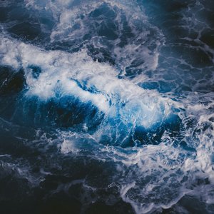 An aerial view of dark ocean waves. The water is indigo blue and white peaks of crashing waves can be seen.