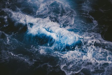 An aerial view of dark ocean waves. The water is indigo blue and white peaks of crashing waves can be seen.