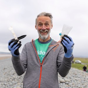A man showing the camera pieces of debris found on the beach. He is holding a plastic fork, an oyster peg, some string, a popper and a plastic wrapper