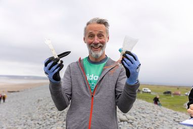 A man showing the camera pieces of debris found on the beach. He is holding a plastic fork, an oyster peg, some string, a popper and a plastic wrapper