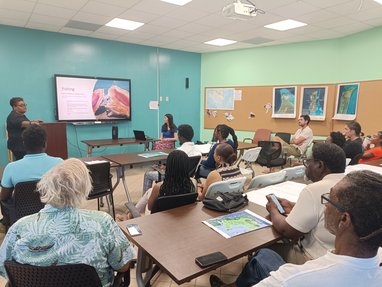 A room of adults listening to a presentation being given. The screen reads "Fishing"