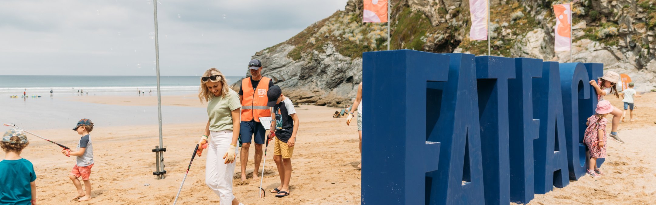 A beach scene with a large sculpture that reads FatFace
