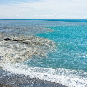 Clean, turquoise sea water near a beach. From the left dark, murky sewage or dirty runoff water is merging creating a dirty mixture between the contrasting blue ocean