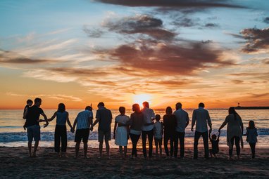 Multiple silhouettes of people on a beach. The setting sun is behind them causing the silhouettes