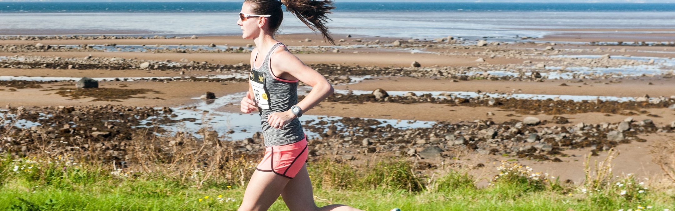 A runner on a paved path next to a rocky shoreline and the sea.