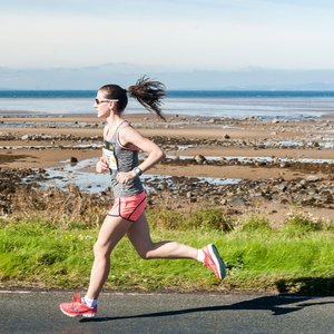 A runner on a paved path next to a rocky shoreline and the sea.