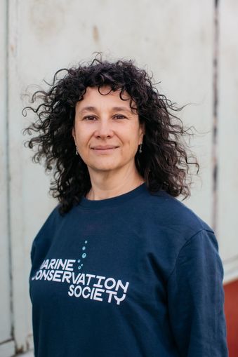 A portrait image of Marine Conservation Society CEO, Sandy Luk, who is standing facing the camera wearing a dark blue Marine Conservation Society top